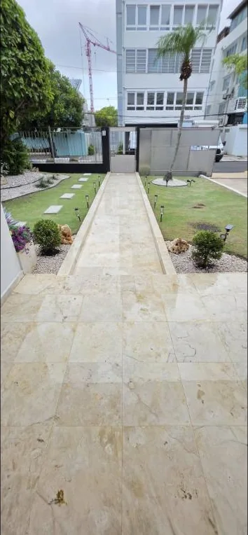 Camino central de mármol entre dos franjas de grama con losas, plantas ornamentales y luces de jardín
