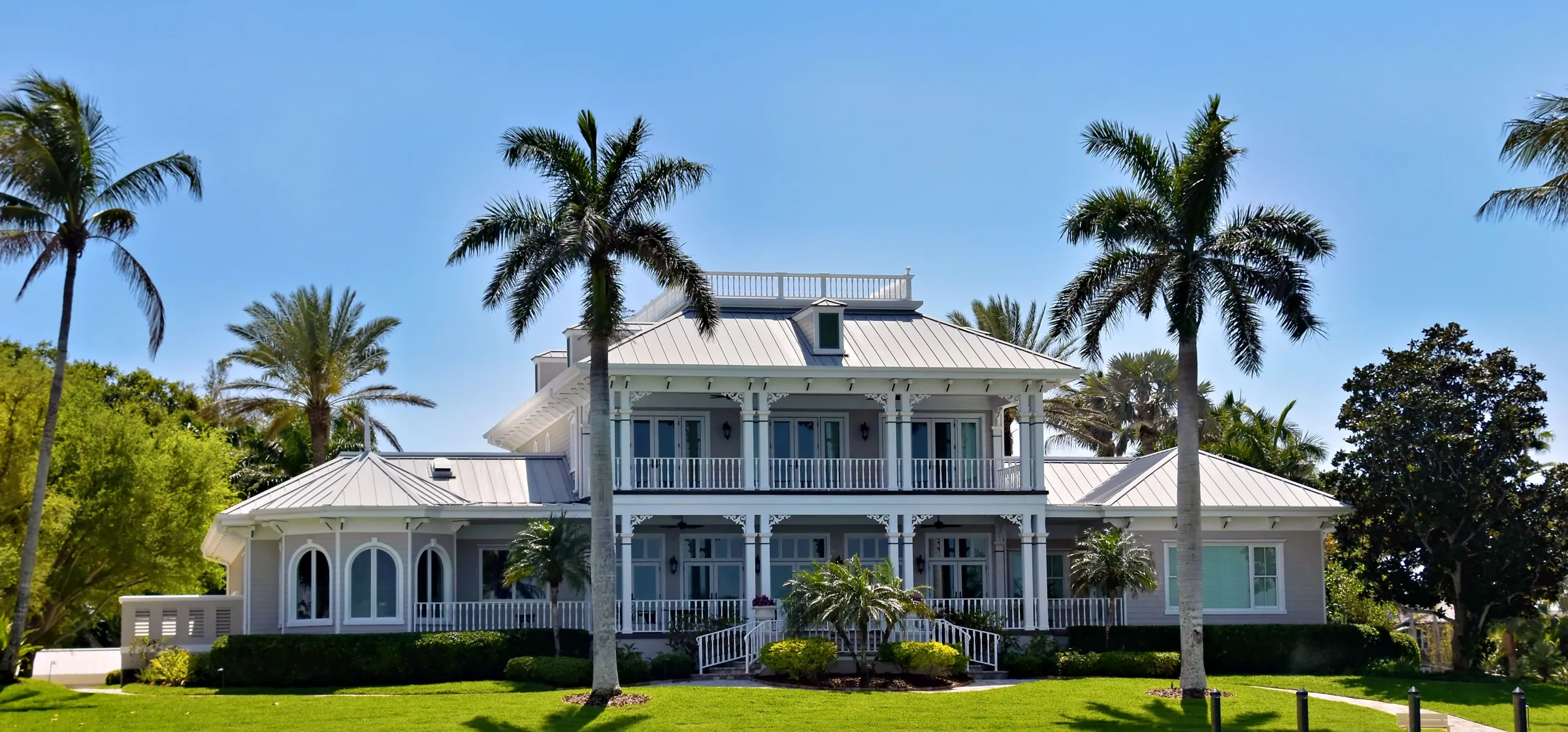 Residencia costera de gran tamaño con grama impecable, palmeras reales y setos podados al frente