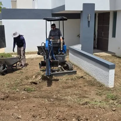 Dos empleados de Fine Lawn trabajando con una mini excavadora nivelando terreno junto a una casa moderna